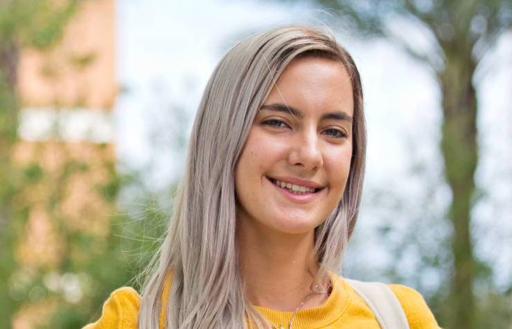 Student outside in yellow sweater wearing a backpack.