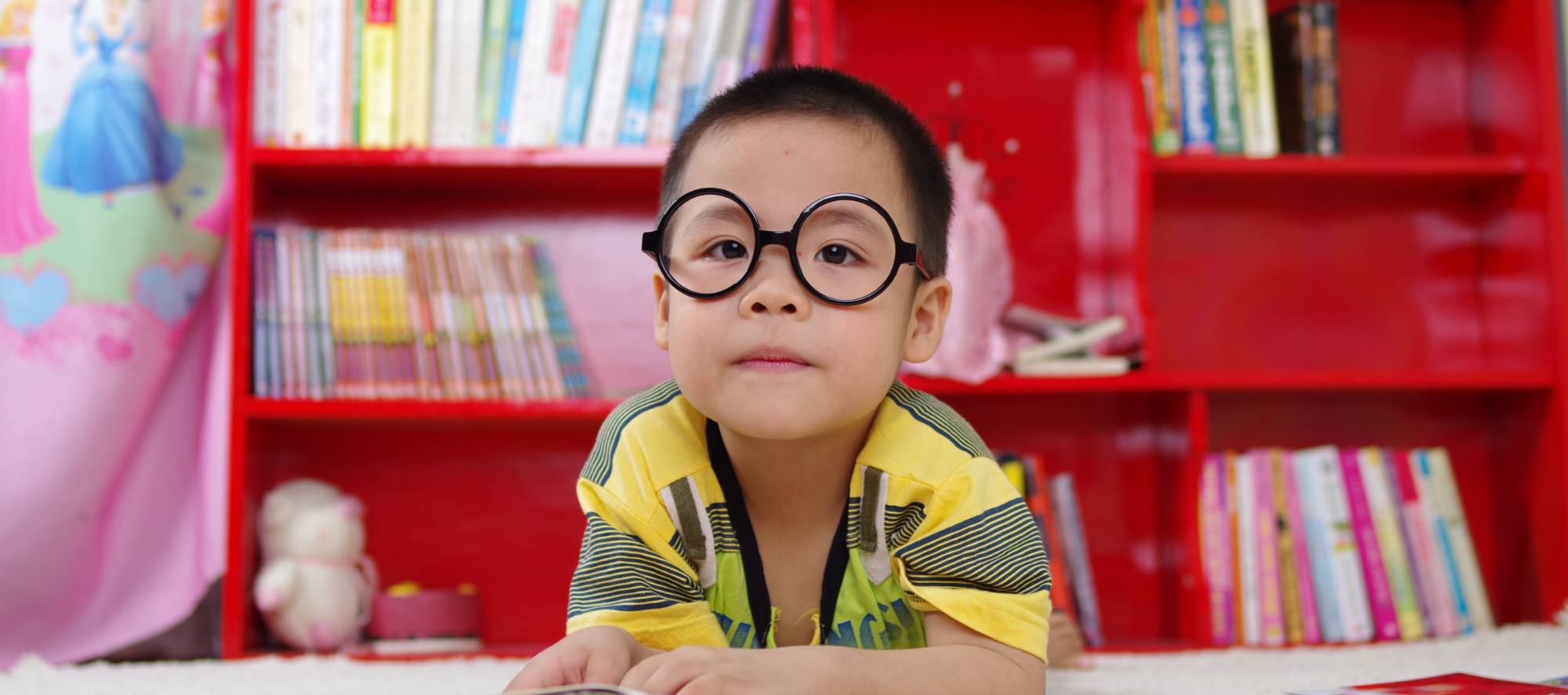 child wearing glasses in front of a bookshelf