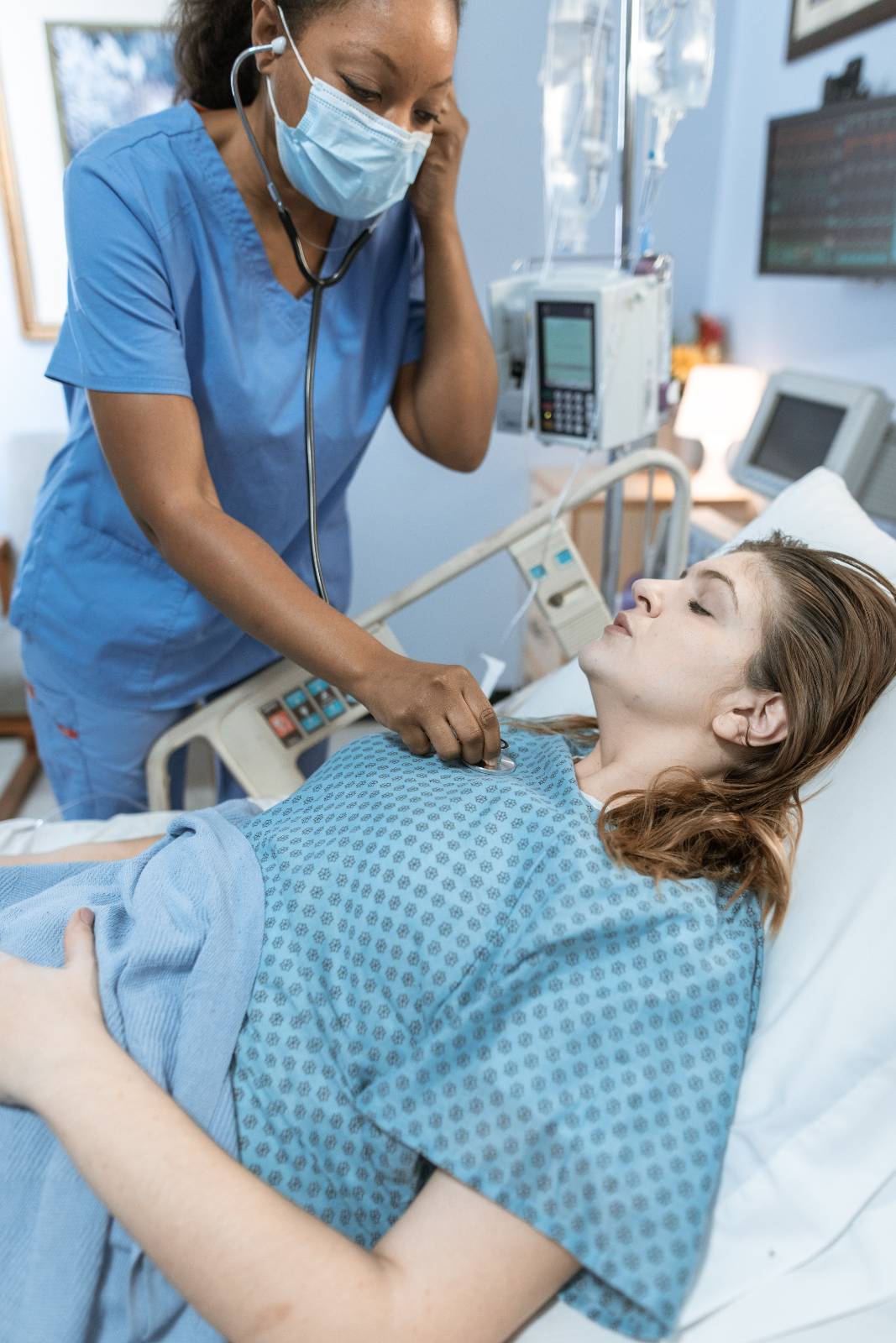 nurse wearing face mask with a patient in hospital bed