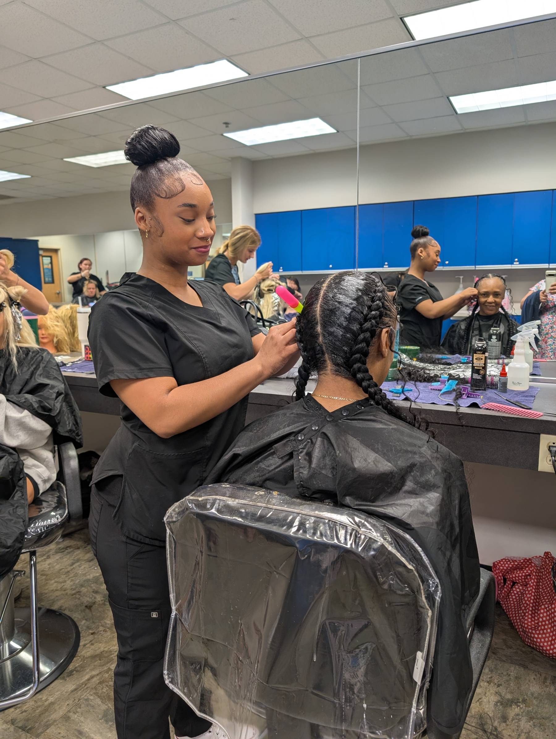 A cosmetology student styling a client's hair in the classroom salon. 