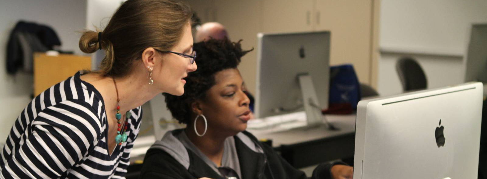 person in black hoodie at computer with person in striped shirt