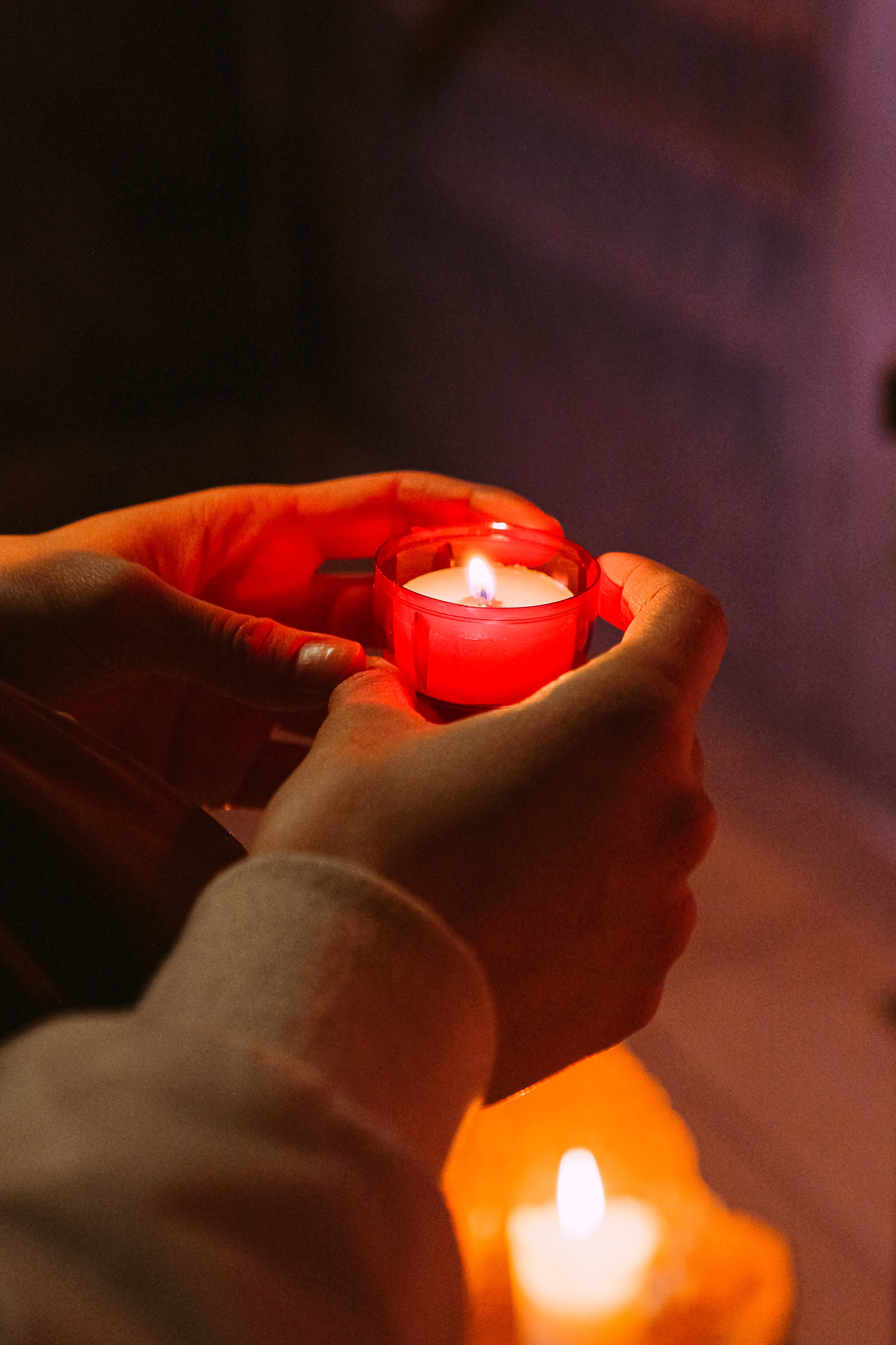 persons hands holding a red candle in a dark room