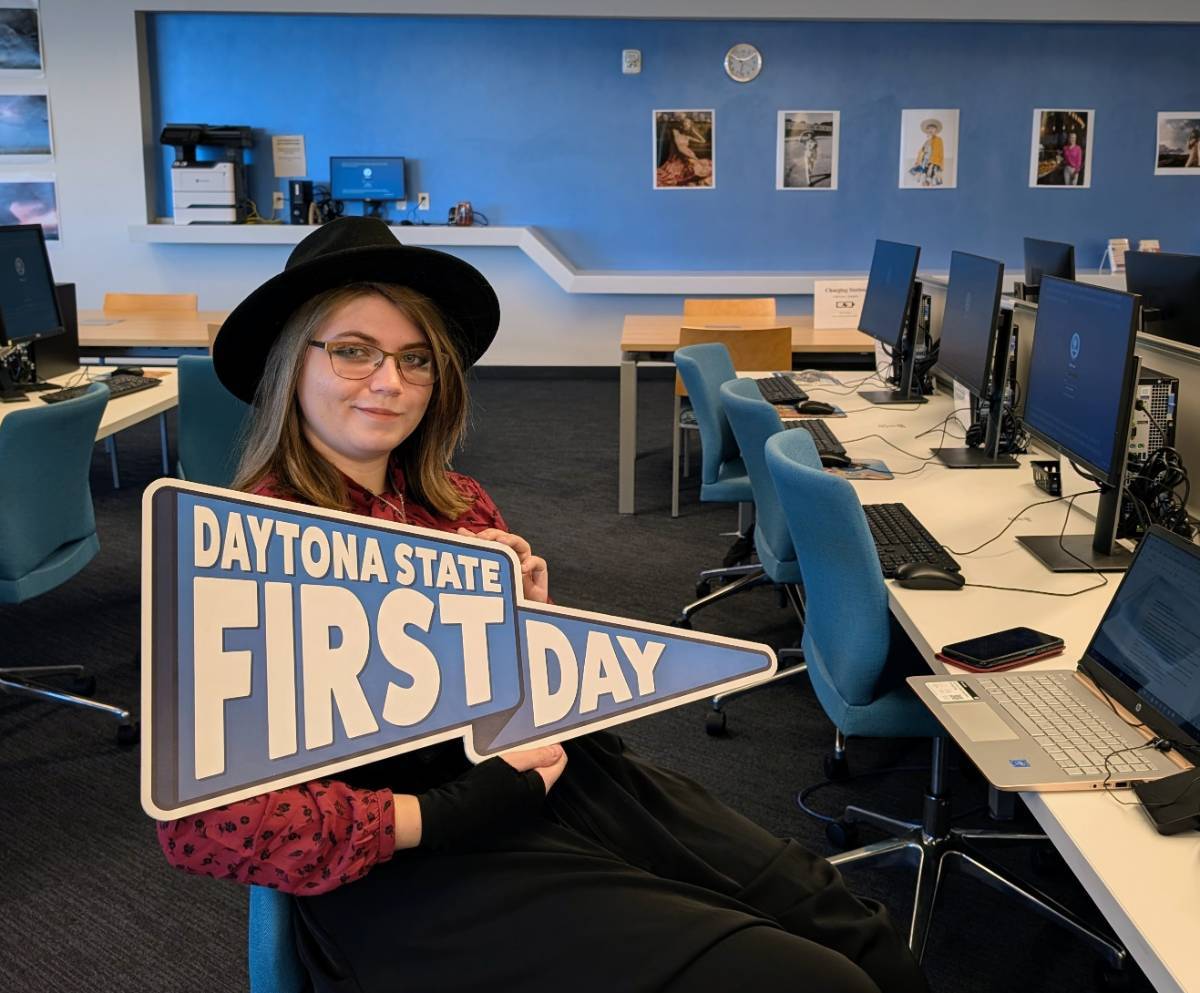 A student holding a Daytona State pennant inside the library. 