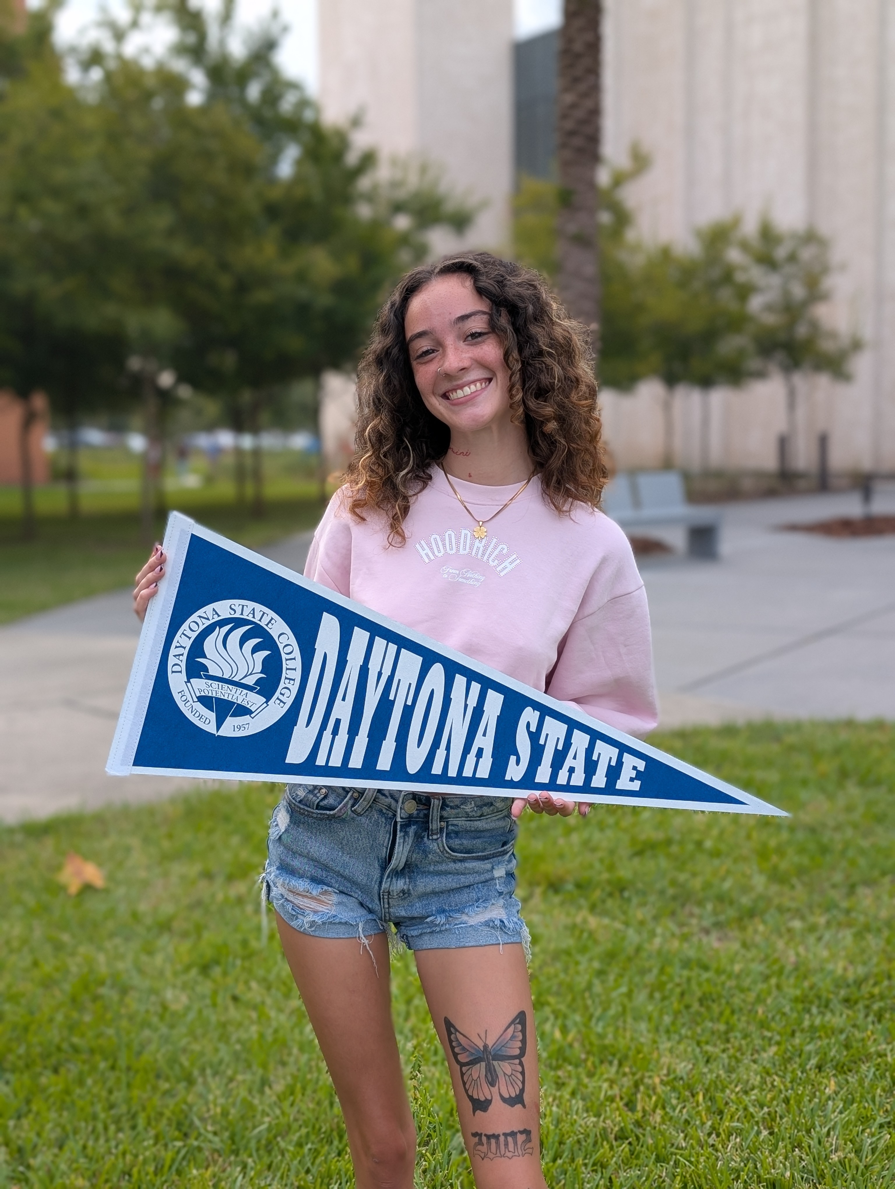 A student holding a Daytona State pennant outside the Student Center. 