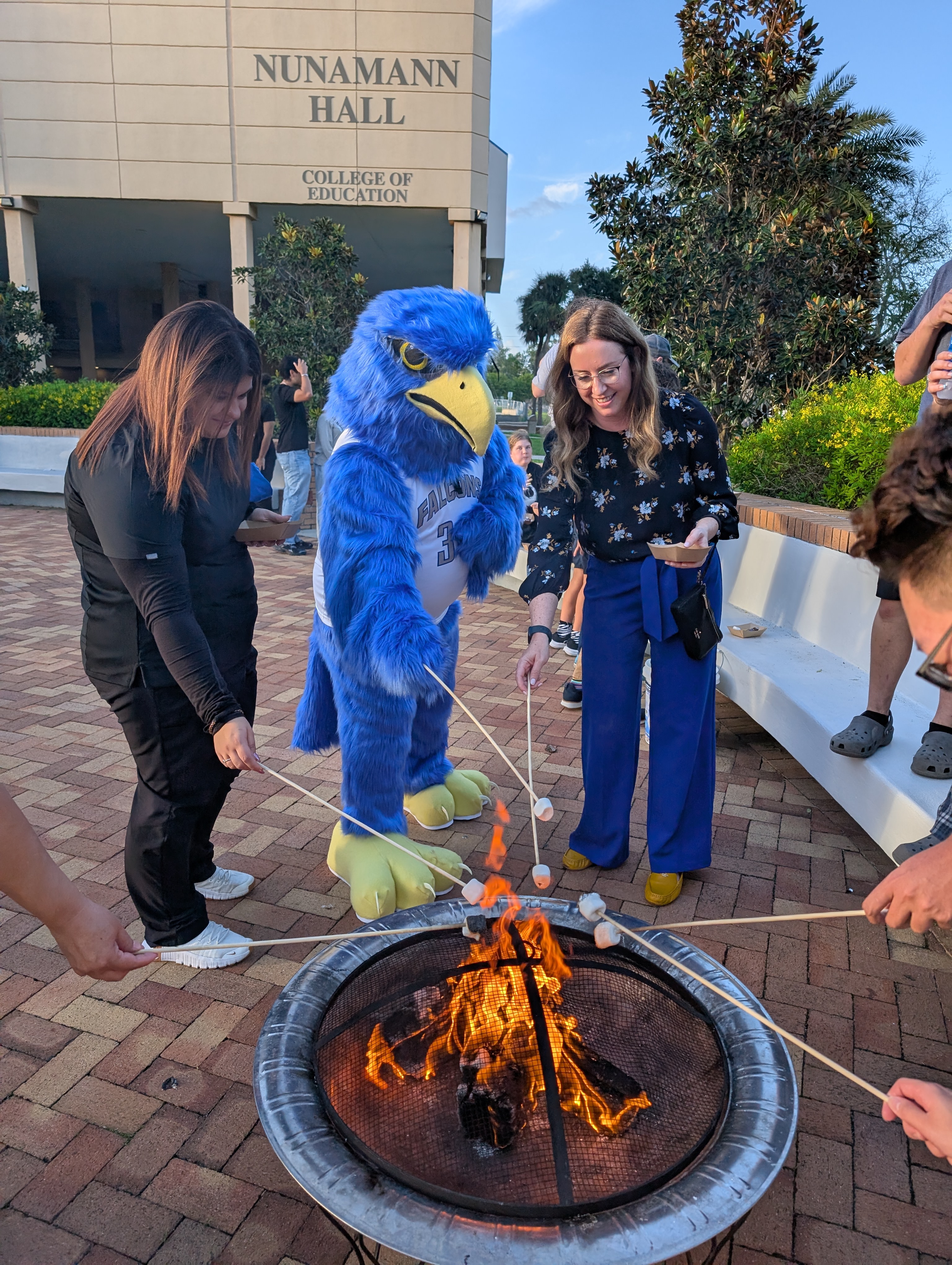 Freddie Falcon roasting a marshmallow over a fire pit during homecoming festivities.