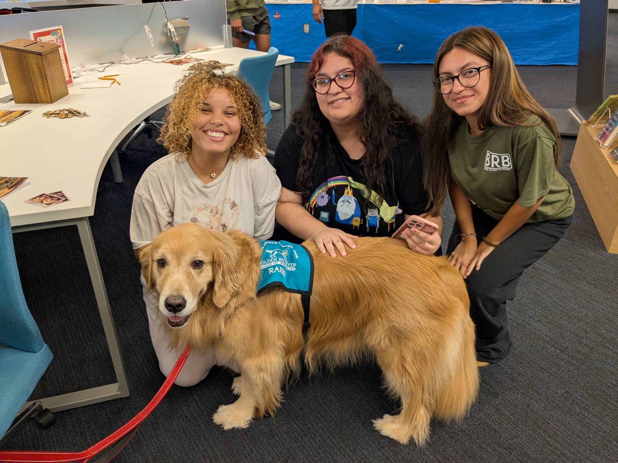 Three students pet a therapy dog in the library during an event. 