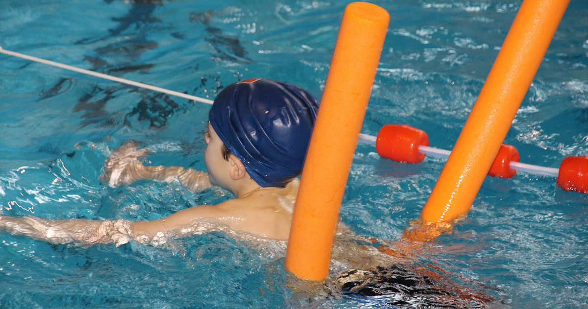 Kid swimming in pool with noodle