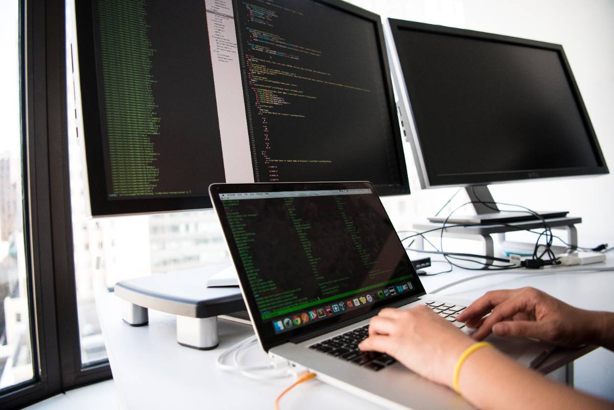 person using a laptop on a desk with multiple monitors