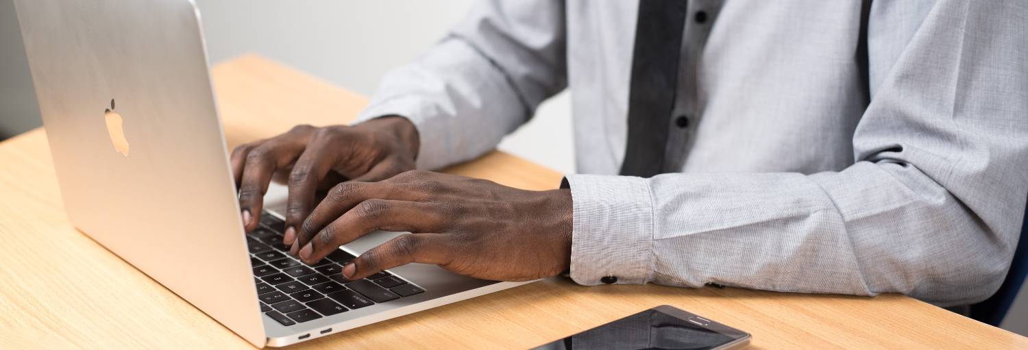 person typing on laptop with cell phone on desk