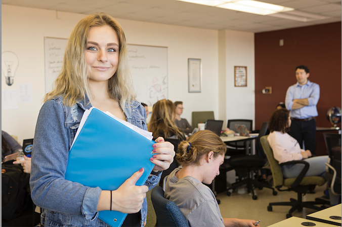 student standing in jean jacket with a notebook