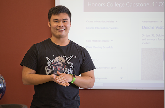 student in black shirt presenting in front of classroom